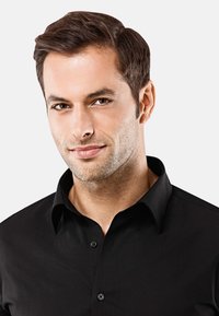 Camicia nera con colletto, chiusura a bottoni e texture liscia, indossata da un uomo con capelli corti e una leggera barba.