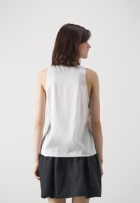 Top senza maniche in satin bianco con una texture liscia, abbinato a una gonna nera a balze. Sul retro presenta un design pulito e minimale.