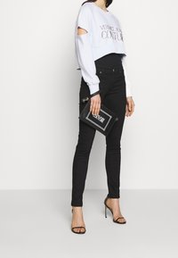 Ljusblå kort sweatshirt med urklippta ärmar, prydd med strasstenar, i kombination med svarta slimmade jeans och svarta sandaletter med remmar.