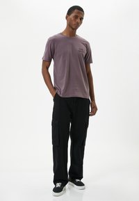 Kortärmad mauve t-shirt med textdetalj framtill, i kombination med svarta cargobyxor med sidofickor och svarta sneakers.
