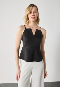 Črn peplum top z V-izrezom, tankimi naramnicami in strukturiranim materialom. Usklajen z belimi širokimi hlačami. Gladka tekstura.
