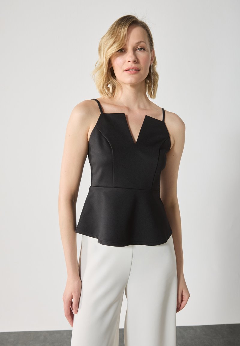 Črn peplum top z V-izrezom, tankimi naramnicami in strukturiranim materialom. Usklajen z belimi širokimi hlačami. Gladka tekstura.