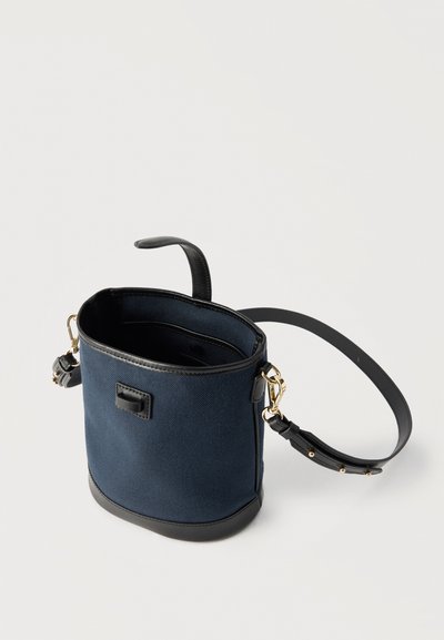 Τσάντα τύπου κάδος σε ναυτικό μπλε χρώμα με μαύρη δερμάτινη επένδυση και ρυθμιζόμενο ιμάντα ώμου, ανοιχτό πάνω μέρος που αποκαλύπτει το εσωτερικό ύφασμα.