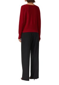 Roter Strickpullover mit gerippter Textur am Saum. Kombiniert mit schwarzen, weit geschnittenen Hosen, sichtbar von hinten.