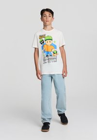 Biała bawełniana koszulka z kolorowymi grafikami postaci z kreskówki, w parze z jasnoniebieskimi dżinsami i czarnymi sneakersami.