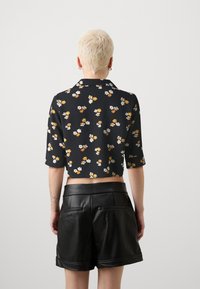 Kuttet svart bluse med blomster mønster i hvitt og oransje, med kragehals og trekvart ermer, kombinert med sorte skinnshorts.