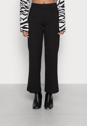 Vrouw die zwarte broek met wijde pijpen, zwarte enkellaarsjes en een cropped top met lange mouwen met een zwart-wit zebrapatroon draagt.