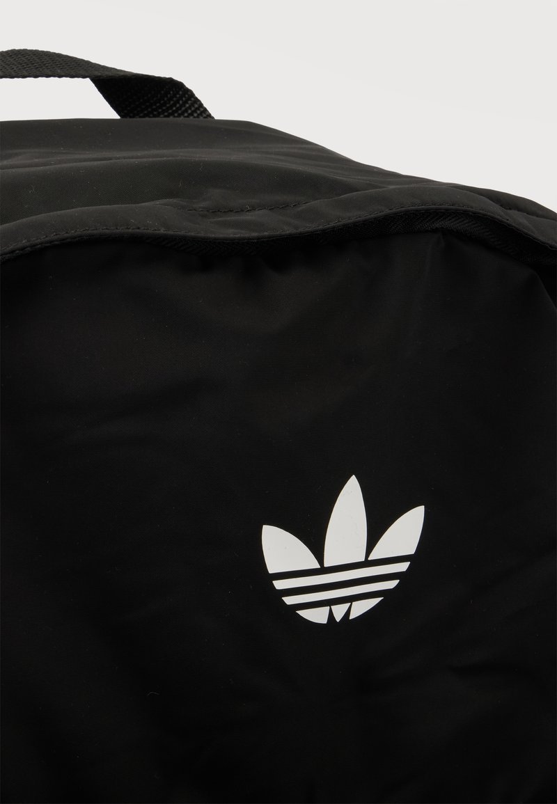 Black fabric backpack with a white Adidas trefoil logo and a black carry handle at the top against a white background.
