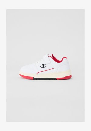 Zapatilla deportiva blanca con acentos rojos, parte superior sintética, correa de velcro, cierre con cordones y suela texturizada con detalles en negro y rojo.