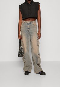 Kort svart pufferväst med hög krage och volangkanter, matchad med ljusblå cargobyxor med flera sidofickor.