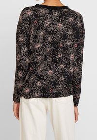 Schwarzes Langarmoberteil mit floralem Muster und weißen sowie rosa Umrissen. Weicher Stoff mit lockerer Passform und rundem Ausschnitt.