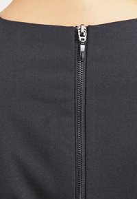 Czarna odzież z centralnym zamkiem z tyłu, o gładkiej fakturze materiału i błyszczącej metalowej hardware.