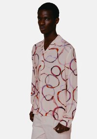 Lange mouwen shirt van lichtroze stof met een cirkelpatroon in verschillende tinten, met een ontspannen kraag en knoopsluiting.