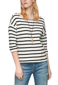 Černobíle pruhované tričko s lodním výstřihem a tříčtvrtečními rukávy, nošené s světle modrými džínami s opotřebením a dlouhým náhrdelníkem s přívěskem.