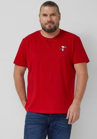 Rotes Baumwoll-T-Shirt mit kurzen Ärmeln und rundem Ausschnitt, mit einer kleinen Snoopy-Stickerei auf der Brust, getragen mit blauen Jeans aus Denim.