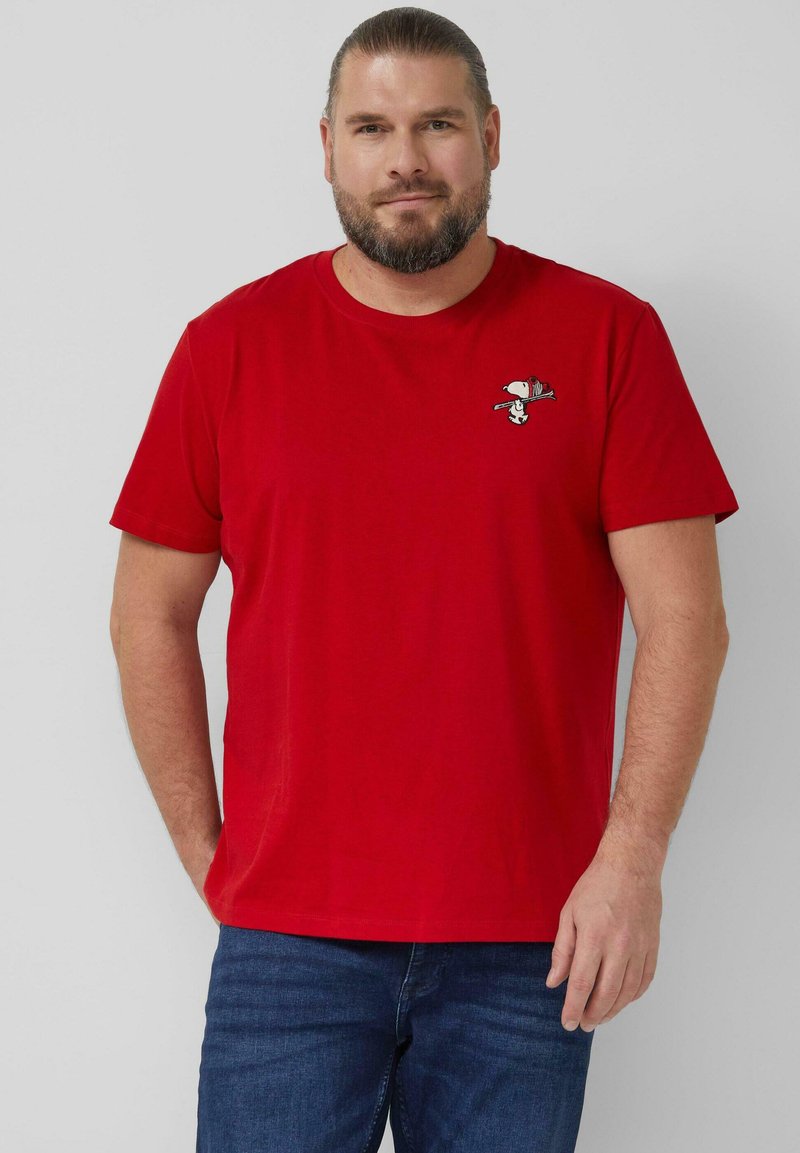 Rotes Baumwoll-T-Shirt mit kurzen Ärmeln und rundem Ausschnitt, mit einer kleinen Snoopy-Stickerei auf der Brust, getragen mit blauen Jeans aus Denim.