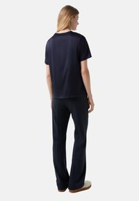 Marineblaues T-Shirt mit kurzen Ärmeln und lockerer Passform, kombiniert mit passenden Hosen, die eine glatte Textur und ein minimales Design aufweisen.