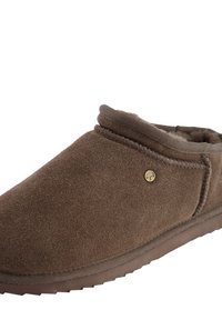 Bruine suede pantoffel met zachte voering, afgeronde vorm, gestikte accenten en een decoratief goudkleurig logo aan de zijkant. Platte rubberen zool.