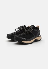 Schwarze Wanderschuhe mit einem Obermaterial aus Mesh, dicker schwarzer Gummisohle, beige Akzenten und gemusterten Schnürsenkeln. "SALEWA"-Logo an der Seite.