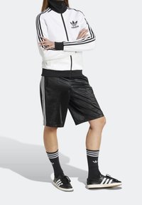 Vit zip-up Adidas träningsjacka med svarta ränder, i kombination med svarta satinhorts med sidostrimmor, svarta strumpor och sneakers.