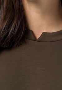 Brun, kortärmad topp i mjukt tyg med rund hals och en liten, sned skärning. Slät yta med minimal sömnad.