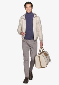 Beige lynlåsjakke over en navy turtle neck, lysegrå bukser og brune sko, holder en taske i tan og creme med brune detaljer.