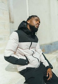 Veste rembourrée noire et rose clair, dotée d'une capuche, d'une fermeture éclair et d'un design en blocs de couleurs. Tissu texturé avec des accents lisses.