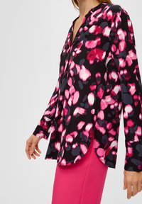 Mujer vistiendo una blusa de manga larga negra con estampado floral abstracto en rosa, blanco y gris, combinada con una falda rosa brillante.