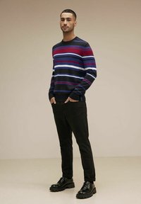 Randig tröja i marinblått, rött och vitt; rund halsringning; bärs med svarta slim-fit byxor och kraftiga svarta stövlar.