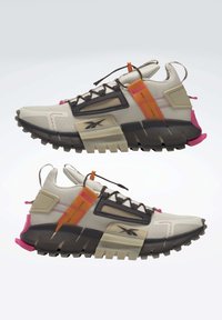 Zapatillas deportivas de color beige claro y negro con suelas gruesas, detalles en naranja y rosa, paneles de malla y bucles para el cordón, mostradas desde vistas laterales.