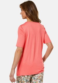 Koraalroze t-shirt met korte mouwen, een relaxte pasvorm en een ronde halslijn, gemaakt van zacht materiaal. Draagt met gebloemde, patronenbroek.