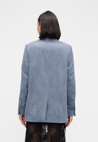 Blauwe corduroy blazer met een notched revers, enkele achtersplit en manchetknoopjes, gecombineerd met een doorschijnende zwarte rok.