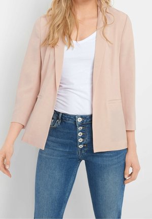 Woman wearing light pink blazer with three-quarter sleeves, white V-neck shirt, and high-waisted blue jeans with five buttons visible.