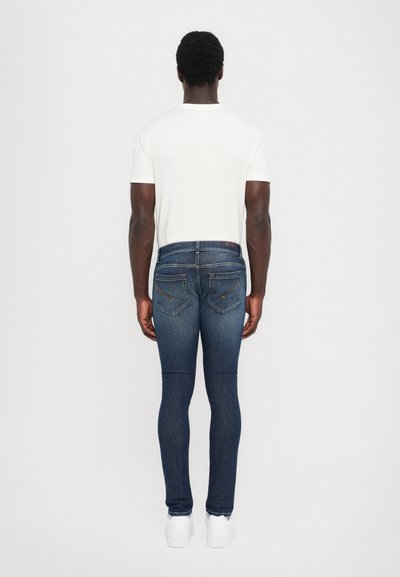 Sittande mörkblå denimjeans med bakfickor. Bärs med en enkel vit t-shirt och vita sneakers. Slät textur, klassisk design.