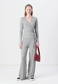 Top wrap rayé gris et blanc à manches longues, associé à un pantalon large assorti, un sac à épaule rouge et des baskets noires.