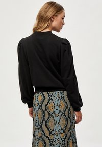 Crna dukserica s napučenim rukavima, rebrastim manžetama i okruglim izrezom. Nosi se preko suknje s uzorkom u plavoj i zlatnoj boji s motivom zmije.