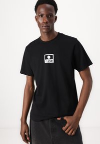 Black cotton t-shirt with a round neckline and short sleeves. Features a white graphic print in the center depicting abstract shapes.