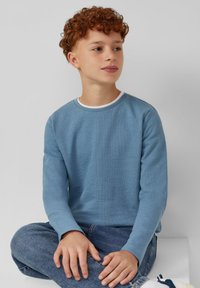 Lichtblauw langetermijnshirt met een gestructureerde stof en een ronde halslijn, gecombineerd met denim jeans. Het shirt heeft een witte accenten bij de kraag.
