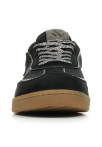 Zwarte sneaker met glinsterende zilveren veters, grijze tonglabel met zwart logo, en bruine rubberen zool, vooraanzicht op witte achtergrond.