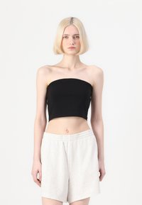 Svart croppad topp utan axelband som är ihopparad med ljusgrå shorts med elastisk midja, slät yta, minimalistisk design och figursydd silhuett.