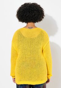 Langärmliger, lässig geschnittener gelber Strickpullover mit weitem Ausschnitt und strukturiertem, offenem Gewebe. Rippenbündchen an Saum und Ärmeln.