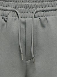 Ceinture élastique grise avec cordon de serrage ajustable sur un pantalon de survêtement en tissu doux, montrant une couture détaillée et une texture.