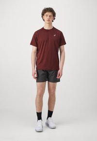 Bordeaux kortermet idretts skjorte med rund hals, kombinert med svarte shorts. Tilbehøret inkluderer svarte sokker og hvite joggesko.