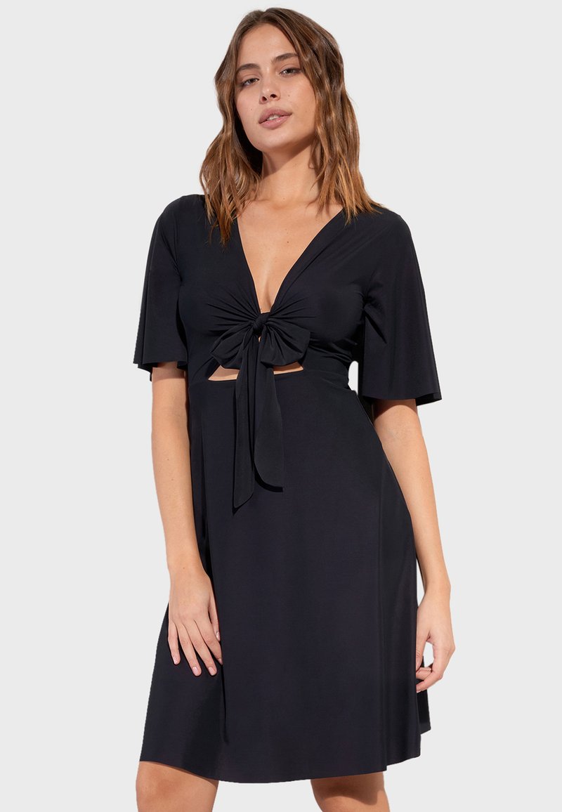 Svart klänning i mjukt material med djup V-ringning, knyt-detalj fram, korta ärmar och utskärningar under bysten.