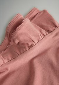 Žíhaná, mäkká látka v tlmenej ružovej farbe so zvlnenými okrajmi a nazbieranými detailmi v páse, ktorá zobrazuje hladkú textúru a pružnosť.