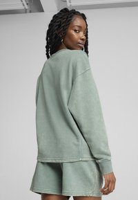 Sweatshirt vert, surdimensionné en tissu doux avec des manches à poignet, associé à un short assorti. Caractéristiques : coupe décontractée et finition décolorée.