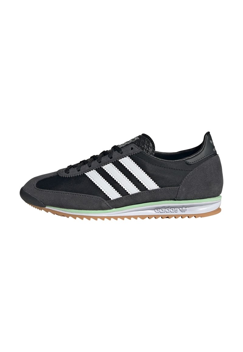 Zapatillas negras y grises con una parte superior de ante y malla, que presentan tres franjas blancas, una suela de goma y un acento verde en la entresuela.
