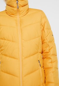 Giubbotto imbottito di un brillante giallo con colletto alto. Presenta cuciture orizzontali e tasche laterali con chiusure a zip per un tocco di dettaglio.