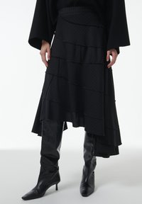 Zwarte gelaagde rok met afwisselend gerimpelde lagen en een streepjespatroon. Gepaarde met kniehoge, puntige zwarte laarzen.