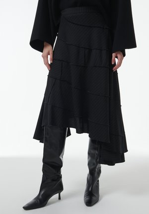 Jupe noire à volants superposés avec des niveaux de fronces alternées et un motif à rayures. Assortie à des bottes noires montantes à bout pointu.